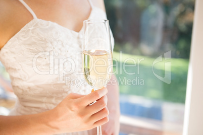Midsection of bride holding champagne while standing by window