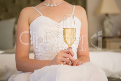 Midsection of bride holding champagne while sitting on bed