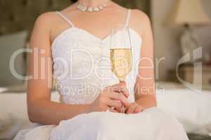 Midsection of bride holding champagne while sitting on bed