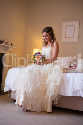 Beautiful bride holding bouquet while sitting on bed