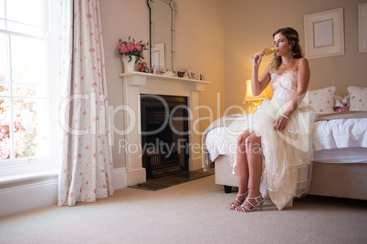 Bride drinking champagne while sitting on bed
