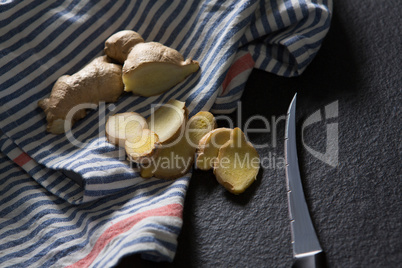 Sliced ginger with knife and napkin on black background