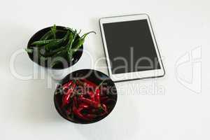 Green and red chili pepper in bowl with digital tablet
