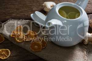 Lemon slice in teapot with ginger and dried orange on wooden table