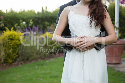 Midsection of newlywed couple embracing in park