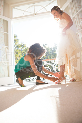 Beautician putting on sandals to bride at home