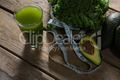Mustard greens, avocado, measuring tape and juice on wooden table