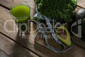 Mustard greens, avocado, measuring tape and juice on wooden table