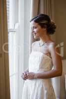 Smiling bride looking through window at home