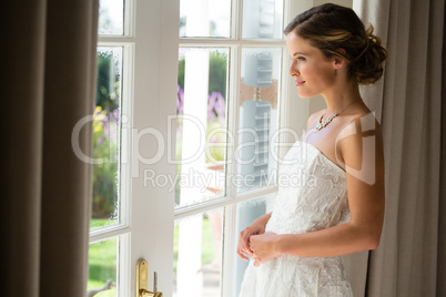 Side view of beautiful bride looking through window at home