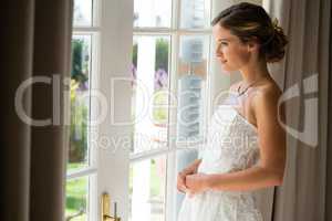 Side view of beautiful bride looking through window at home