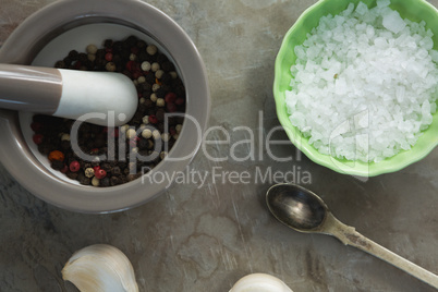 Black pepper in mortar and pestle with bowl of salt and garlic