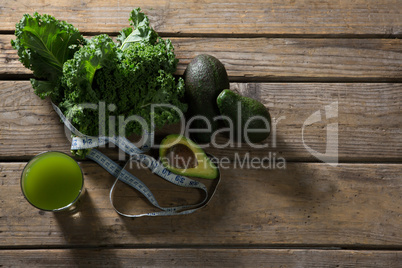 Mustard greens, avocado, measuring tape and juice on wooden table