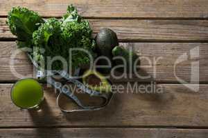 Mustard greens, avocado, measuring tape and juice on wooden table