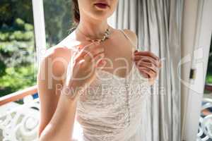 Midsection of bride in wedding dress standing by window