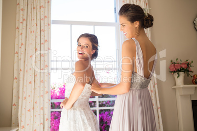 Bridesmaid adjusting bride wedding dress in fitting room