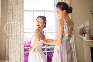 Bridesmaid adjusting bride wedding dress in fitting room