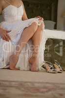 Low section of bride trying sandals while sitting on bed