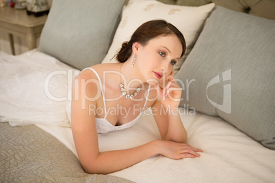 Thoughtful bride relaxing on bed at home
