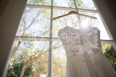 Low angle view of wedding dress hanging on window in room