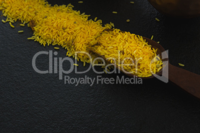 Raw organic yellow rice in wooden scoop over black background