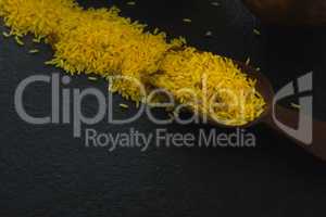 Raw organic yellow rice in wooden scoop over black background
