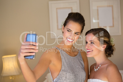 Bridesmaid taking selfie with bride in bedroom