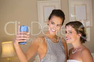 Bridesmaid taking selfie with bride in bedroom