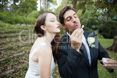 Newlywed couple blowing bubbles in park