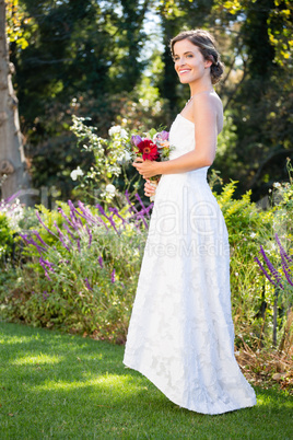 Smiling bride holding bouquet while standing on grassy field