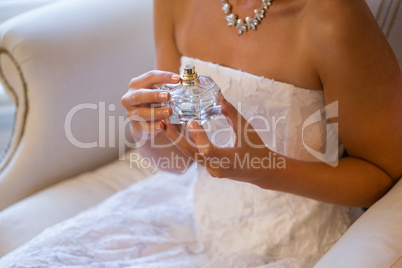 Midsection of bride holding perfume sprayer while sitting on armchair