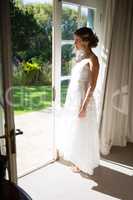 Beautiful bride looking away while standing at doorway in house