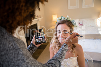 Woman applying makeup to bride in dressing room