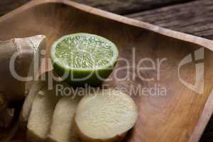 Sliced ginger and halved lemon on wooden tray