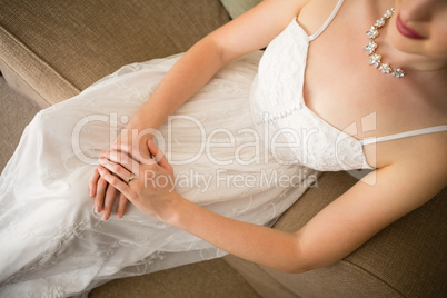 Midsection of beautiful bride in wedding dress sitting on sofa at home