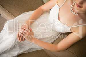 Midsection of beautiful bride in wedding dress sitting on sofa at home