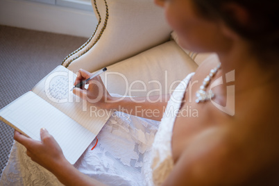 High angle view of beautiful bride writing in diary while sitting on armchair