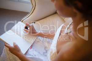 High angle view of beautiful bride writing in diary while sitting on armchair