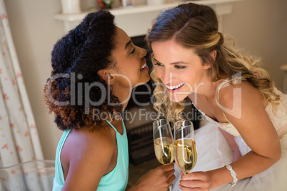 Bridesmaid whispering into bride ear while having champagne