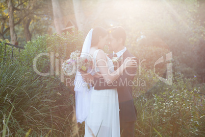 Romantic newlywed couple with eyes closed embracing in park