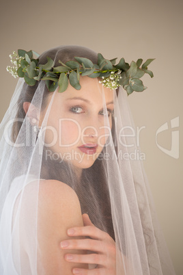 Portrait of beautiful bride in wedding dress and tiara standing by wall at home