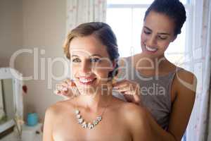 Bridesmaid fastening bride necklace in room