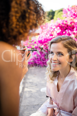 Woman applying makeup to bride in yard