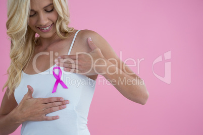 Smiling woman touching breast while looking Breast Cancer Awareness ribbon