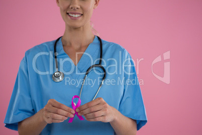 Mid section of happy female doctor in scrubs showing Breast Cancer Awareness ribbon