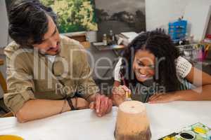Man assisting woman in painting vase