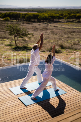 Couple practicing yoga on at poolside