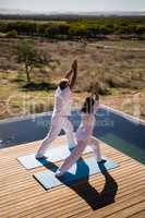 Couple practicing yoga on at poolside
