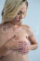 Shirtless woman checking for lumps while touching breast
