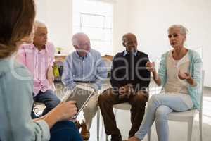 Woman gesturing while sitting with friends and instructor during discussion